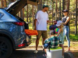 Family with kids remove the camping supplies from car trunk at forest. summer holidays, road trip