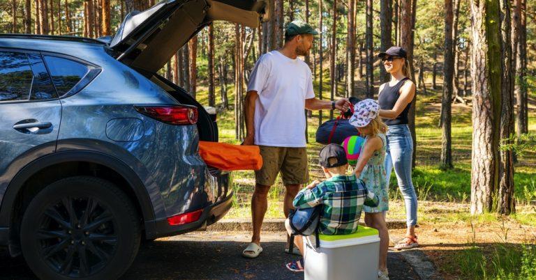 Family with kids remove the camping supplies from car trunk at forest. summer holidays, road trip