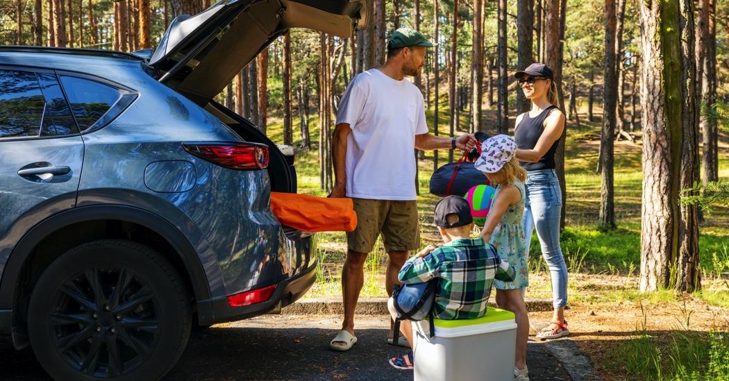 Family with kids remove the camping supplies from car trunk at forest. summer holidays, road trip